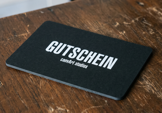 Schwarze canvArt studios Gutscheinkarte mit der Aufschrift Gutschein auf einem Holztisch